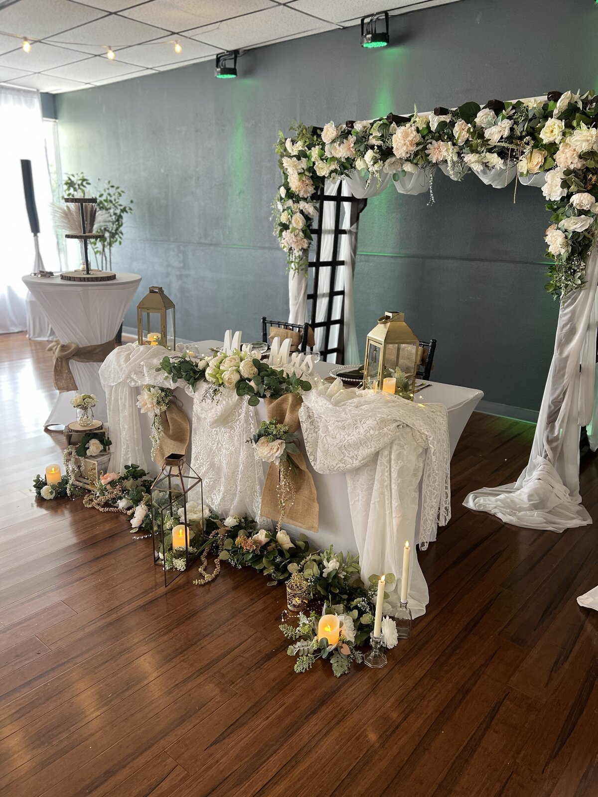 Rustic chic wedding reception headtable at our Clearwater, Florida event venue, The District - Inclusive decor package featuring a wooden arbor arch with a combination of lace and burlap for an elegant indoor celebration