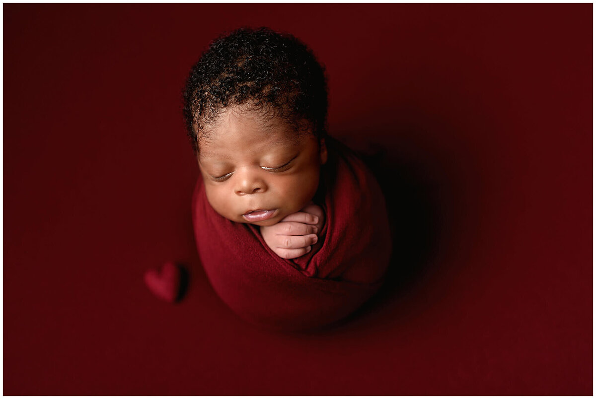Newborn baby boy studio session in red wrap and heart.