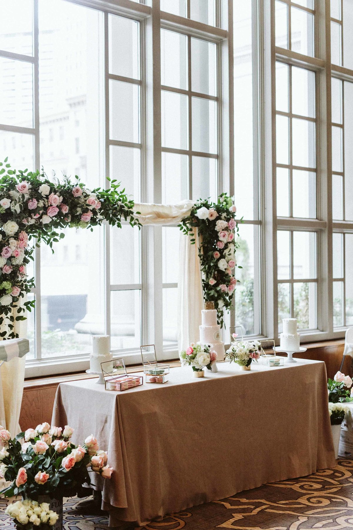 long table in front of flower greenery arch in front of tall window