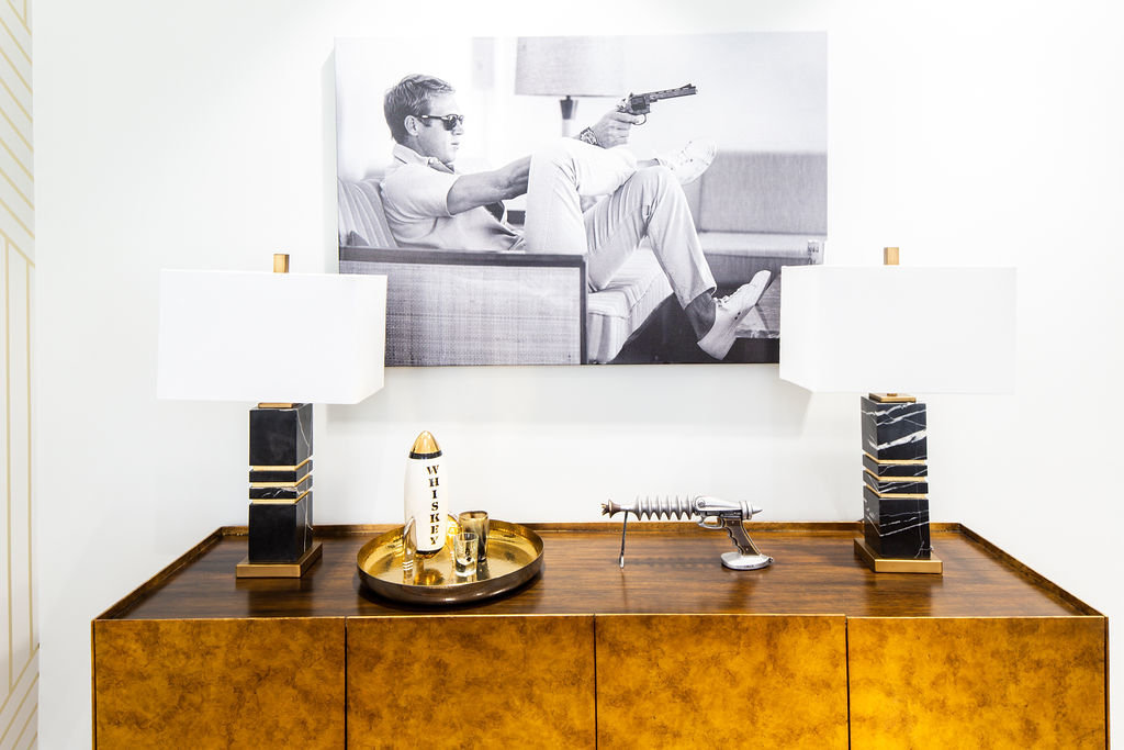 Masculine man cave office with Steve McQueen black and white art, black marble table lamps, and gold credenza