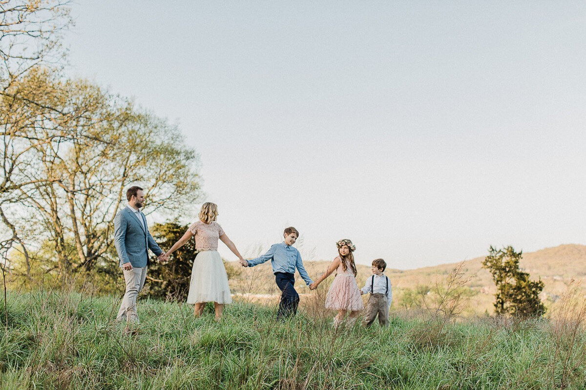 Family of five walks single file holding hands on scenic hillside in family portrait