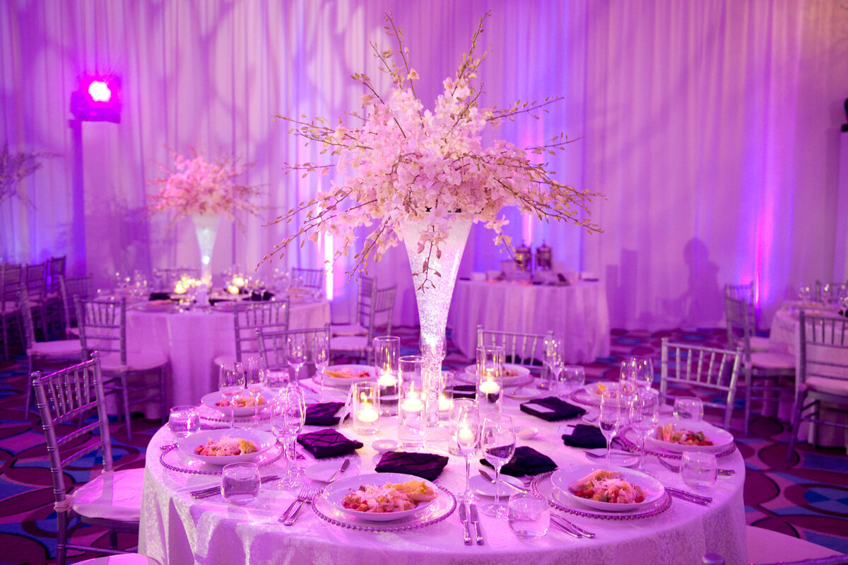 Wedding reception tables with chairs, dinnerwares, candles and floral centerpieces