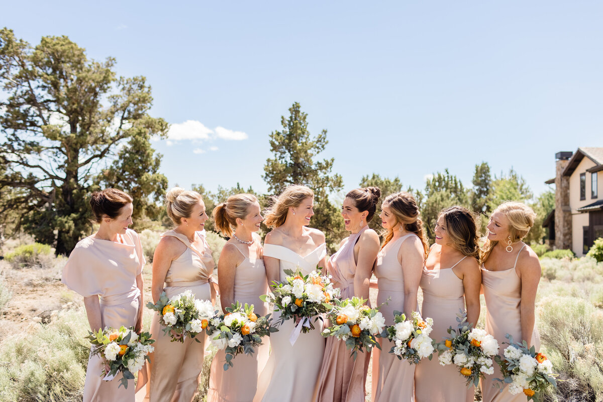 Bride with bridesmaids at Pronghorn Resort holding bouquets of white flowers with orange ranunculus and juniper