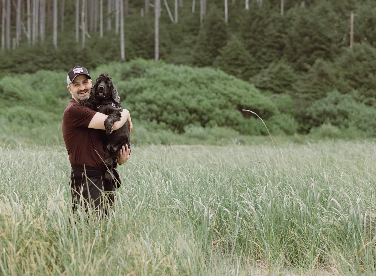 Tony Asgari holding his dog in a grassy field.