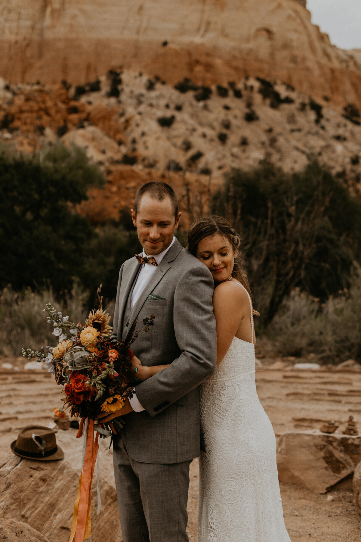bride and groom standing in front of red rocks at Ghost Ranch