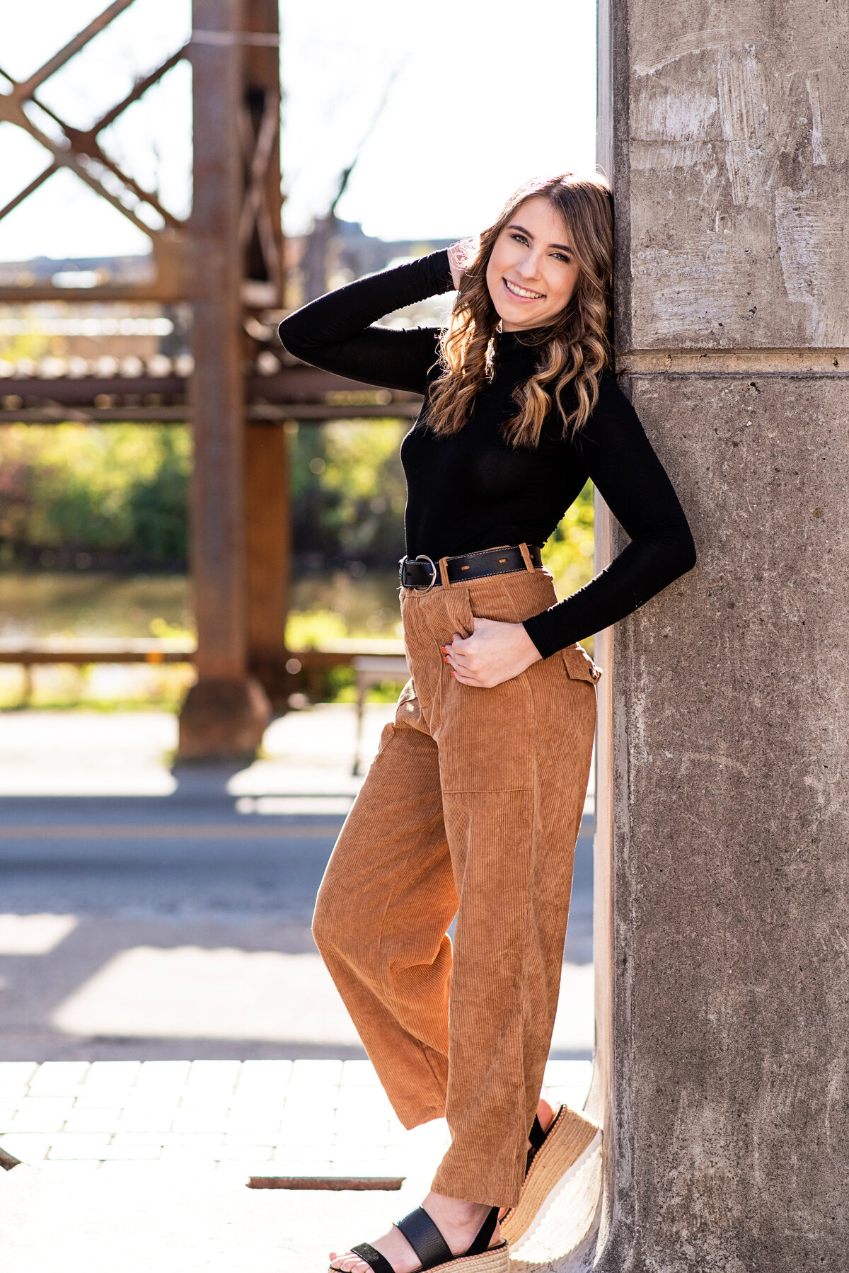 Fall senior portrait session for Richmond high school senior girl in downtown Richmond, VA. Bella is wearing brown pants and a black turtleneck and posing at the flood wall.