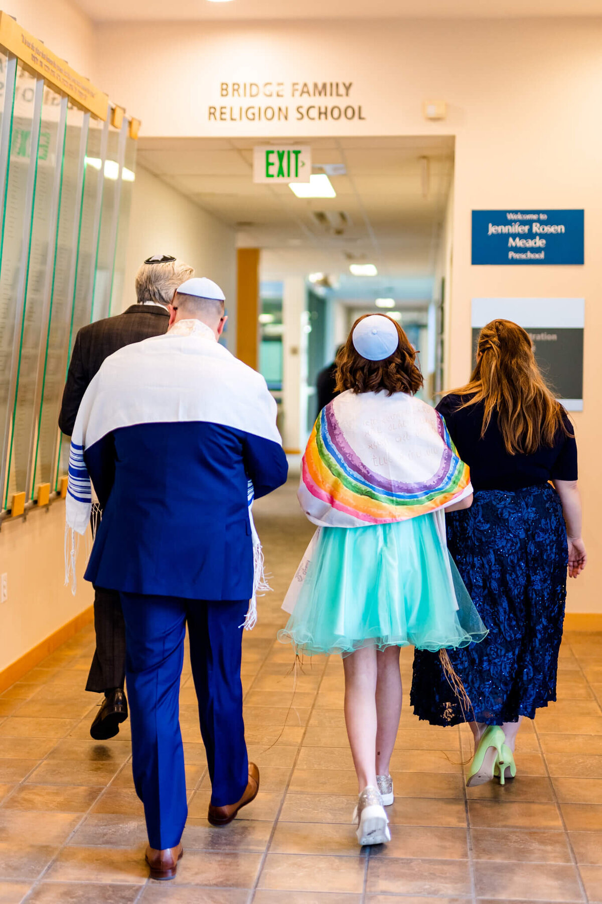 A teenage girl walks through the temple with mom, dad and the rabbi for her mitzvah in a rainbow tallit