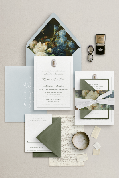 A classic wedding invitation suite displayed against a soft sand-coloured background. The main invitation, printed on textured ivory cardstock, features elegant calligraphy and a dainty thin line border. An elongated white wax seal with gold ink floral details adorns the main invitation, while the main envelope and RSVP envelopes showcase muted green and blue tones matching the vintage painting envelope liner and vellum belly band.