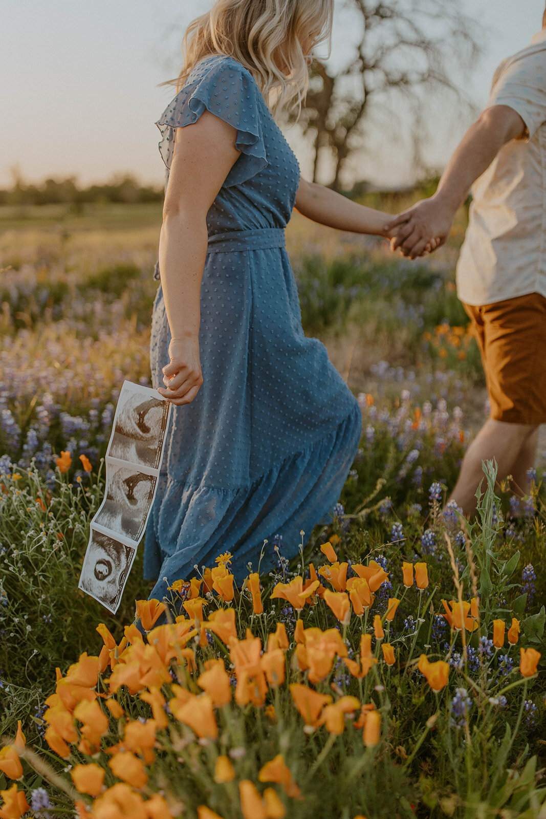 mom to be holds sonogram photo in field of wildflowers