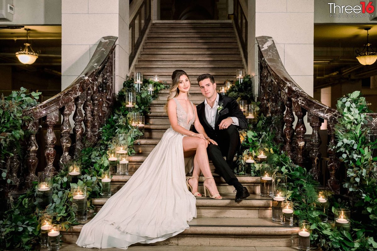 Bride and Groom sit together on the steps of a staircase surrounded by decorative candles
