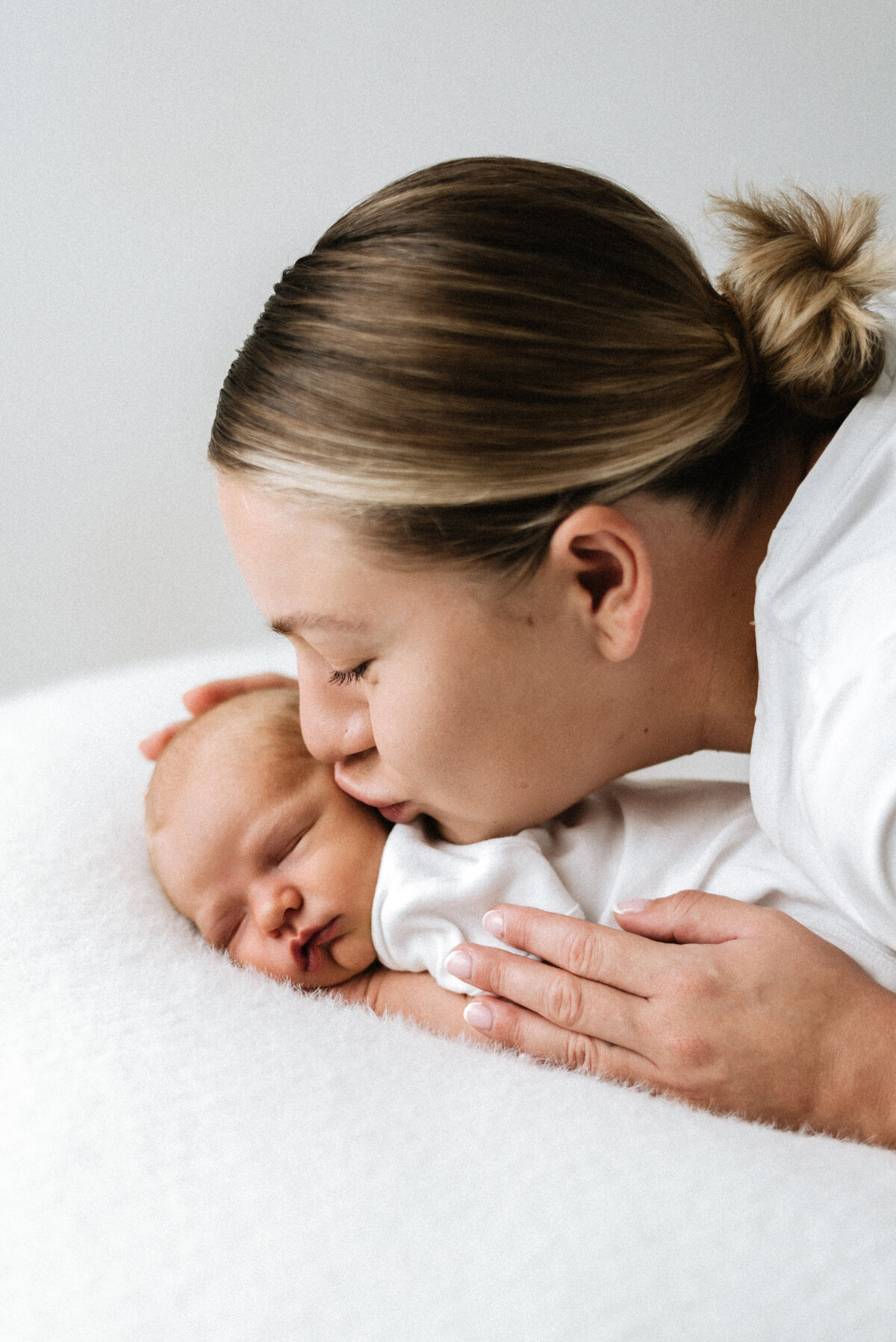 A mother kissing her newborn baby in billingshurst newborn photoshoot