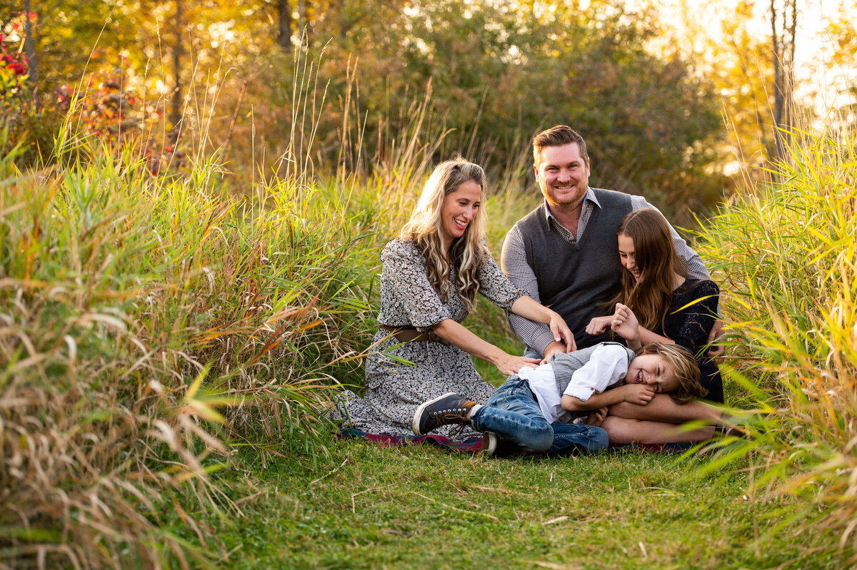 mom and dad tickling their children on a blanket during their golden hour sunset session taken by Ottawa family photographer JEMMAN Photography