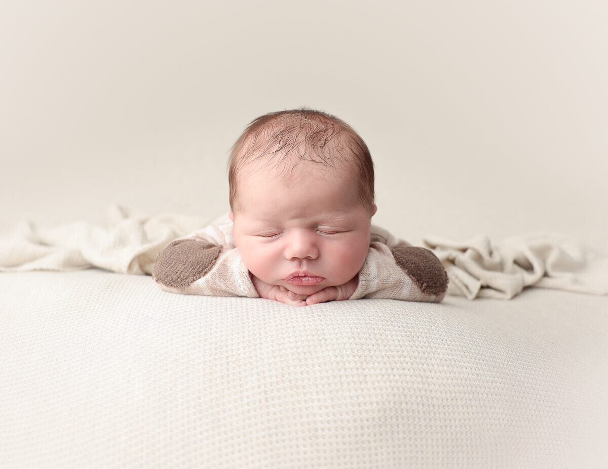 Newborn boy in a head-on-hands pose, peacefully resting in a cozy studio setting, showcasing portrait photography in Rochester, NY.