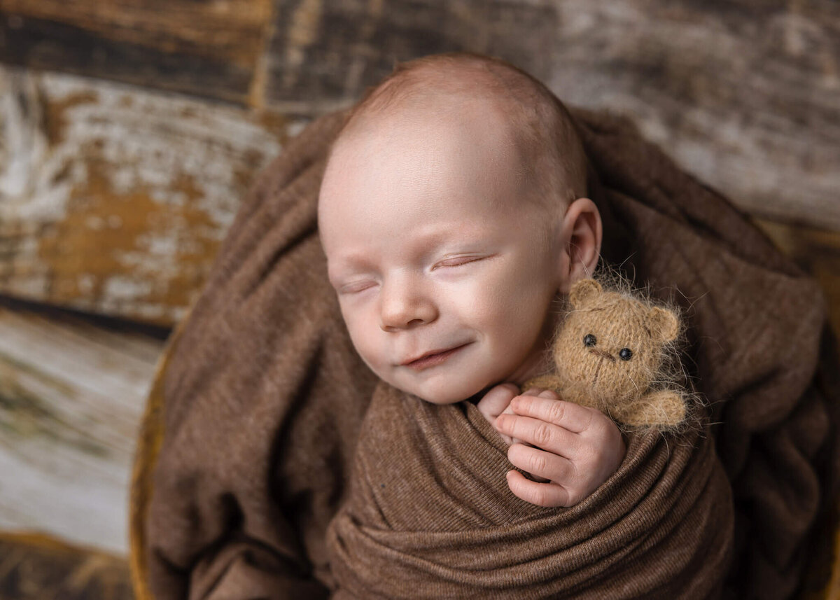 smiling newborn baby asleep holding a tiny teddy bear