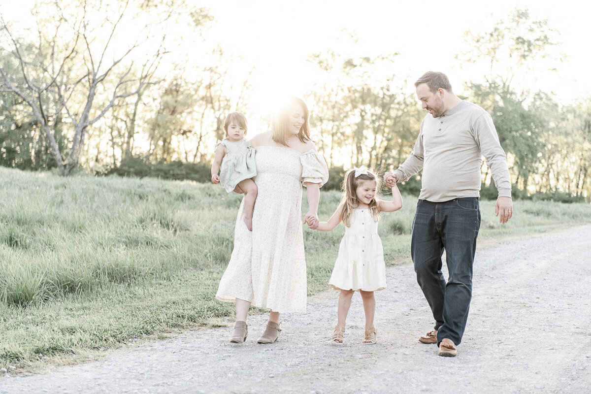 a family with 2 young children hold hands and walk in a field at sunset  in Thompson's Station TN by Nashville family photographer