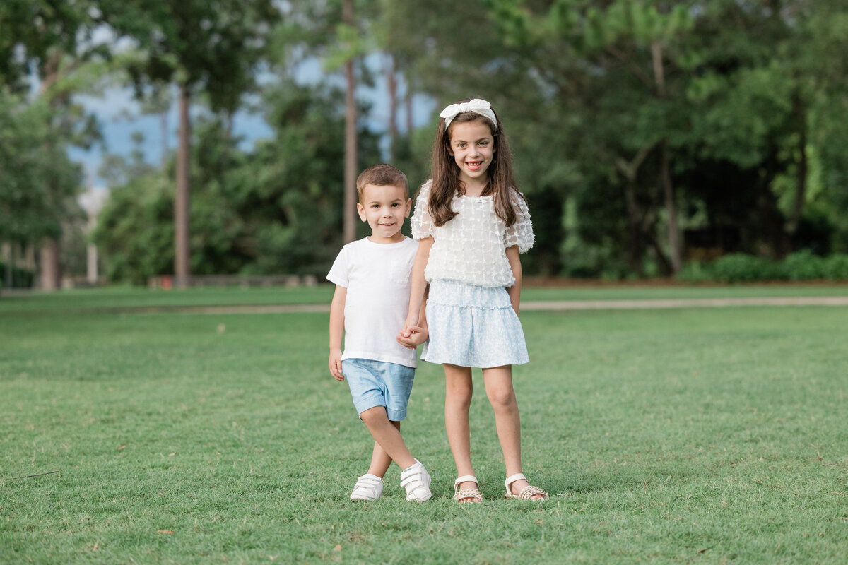 Two siblings standing in the grass holding hands