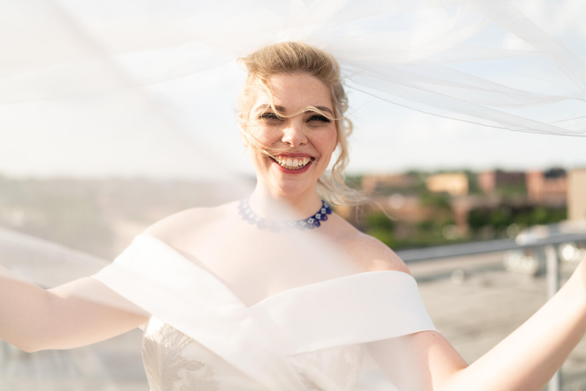 Bride holds out veil and laughs on the roof of the reception venue.