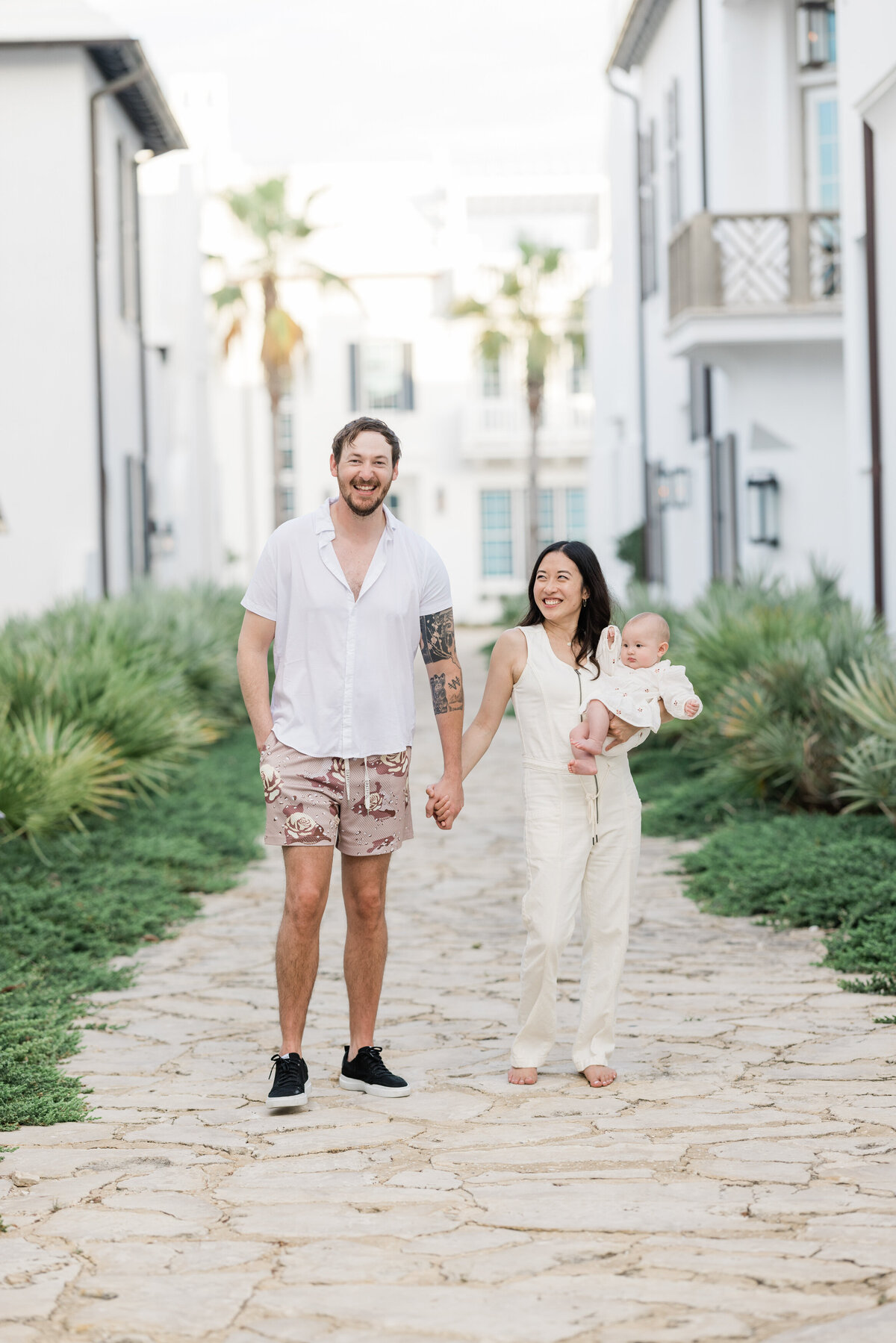 A couple holding hands and walking together as one holds a baby in Alys Beach Florida.