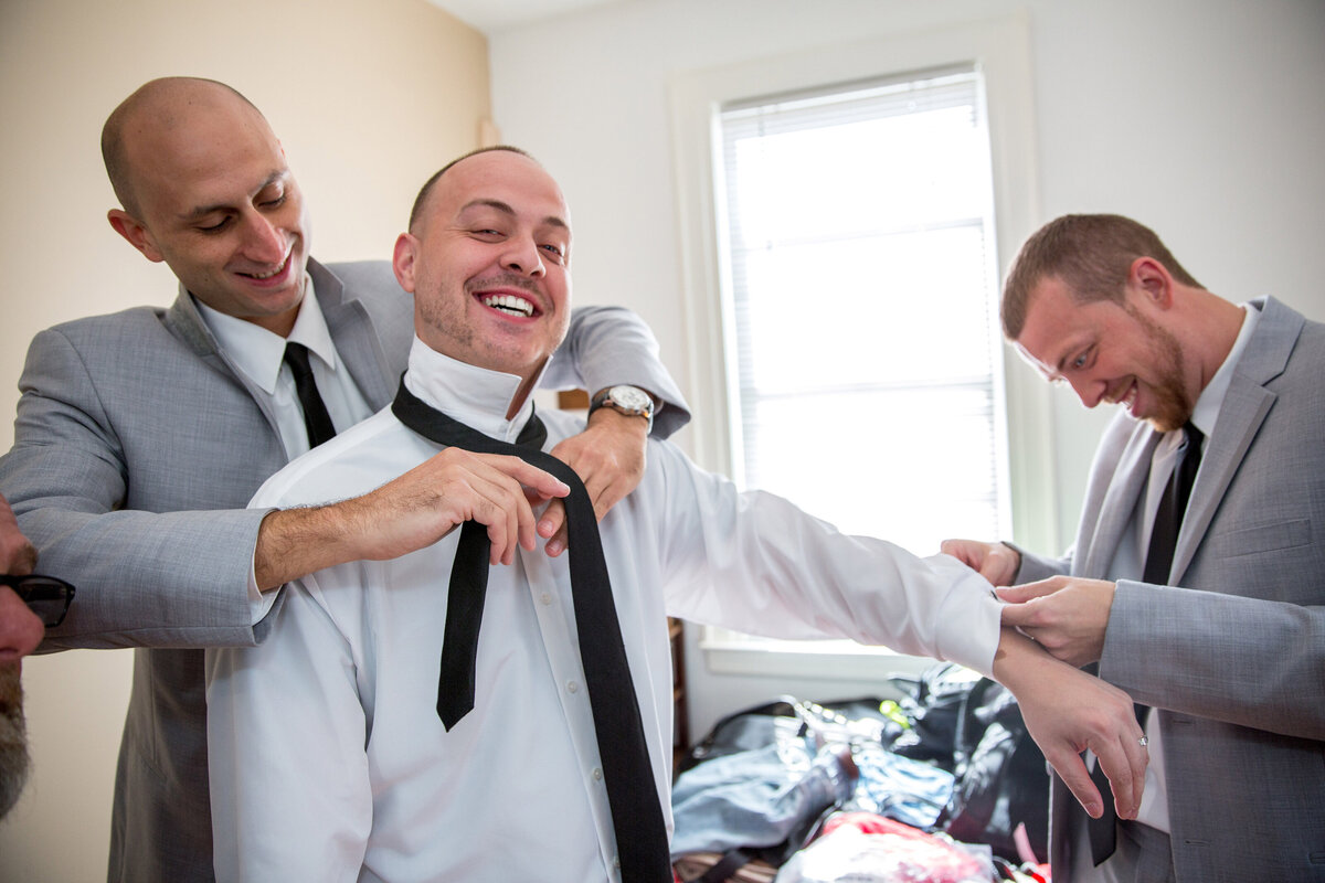 Two men helping a groom get dressed.