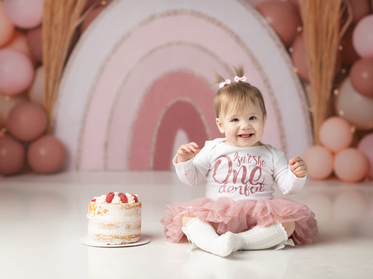 one year old girl sitting next to cake for cake smash photography cleveland family photographer