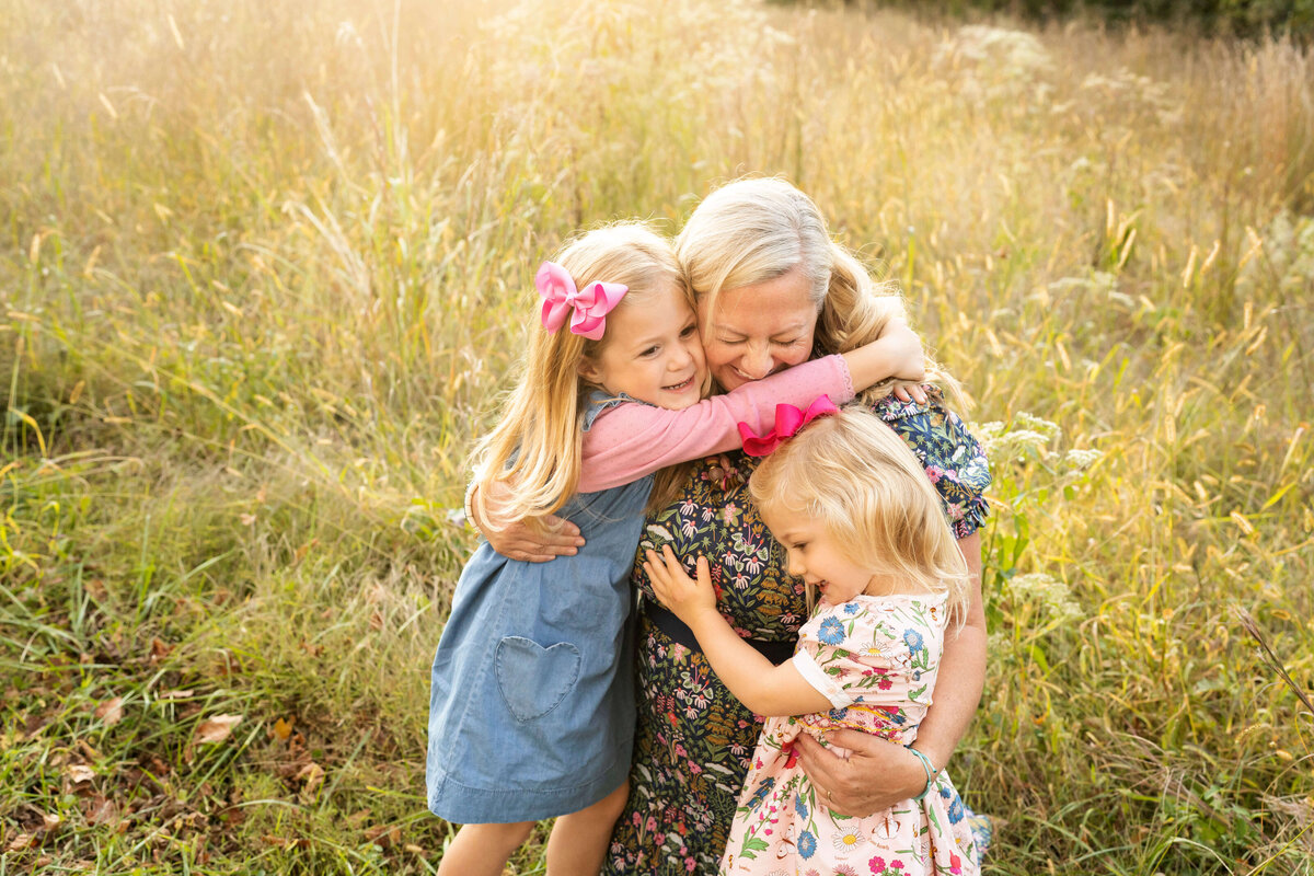 Mother hugging 2 young daughters in field by Atlanta family photographer