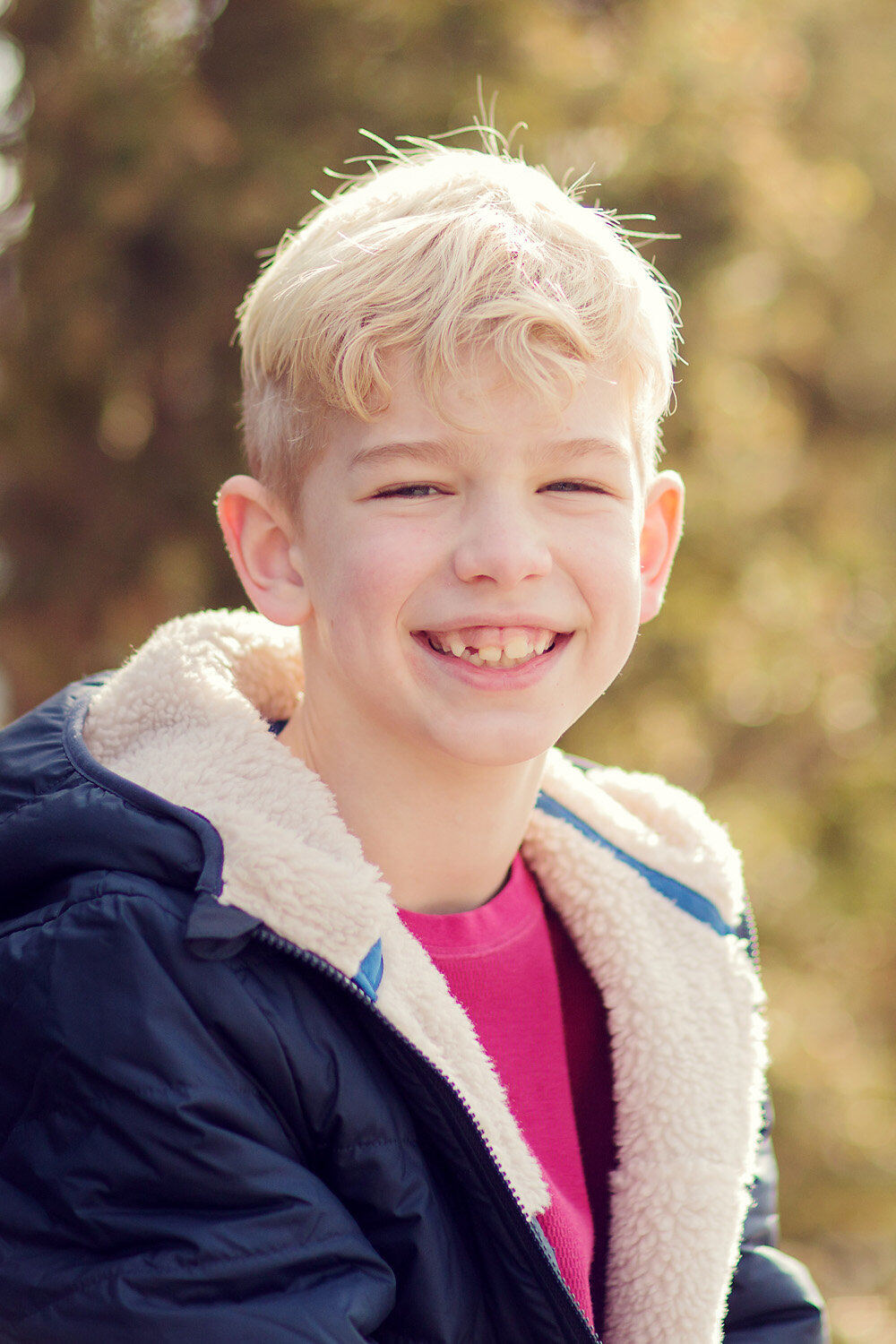 Tween boy with blonde hair smiling at the camera in a blue coat.