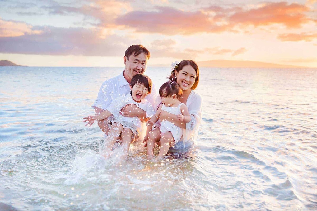 Family fully clothed splashing in the ocean with Love + Water during their sunset portraits in Wailea