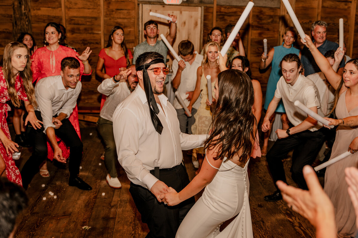 The couple has fun during their wedding dance floor in the barn at Machias Meadows in Snohomish, Washington. Groom wears a tie tied around his forehead.