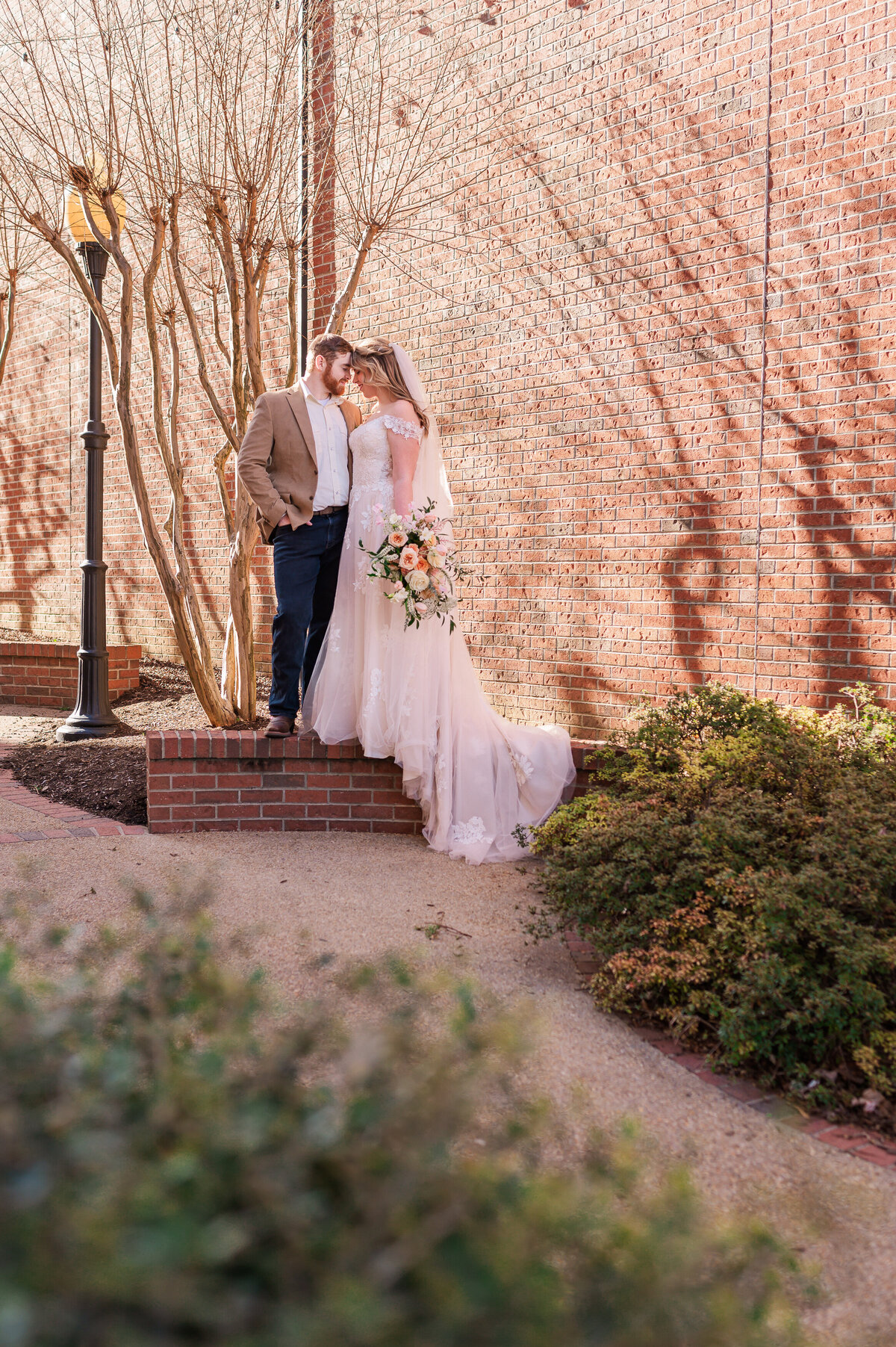 A happy couple standing on a brick wall during sunset in Downtown Oxford enjoying their Raleigh wedding photography by JoLynn Photography