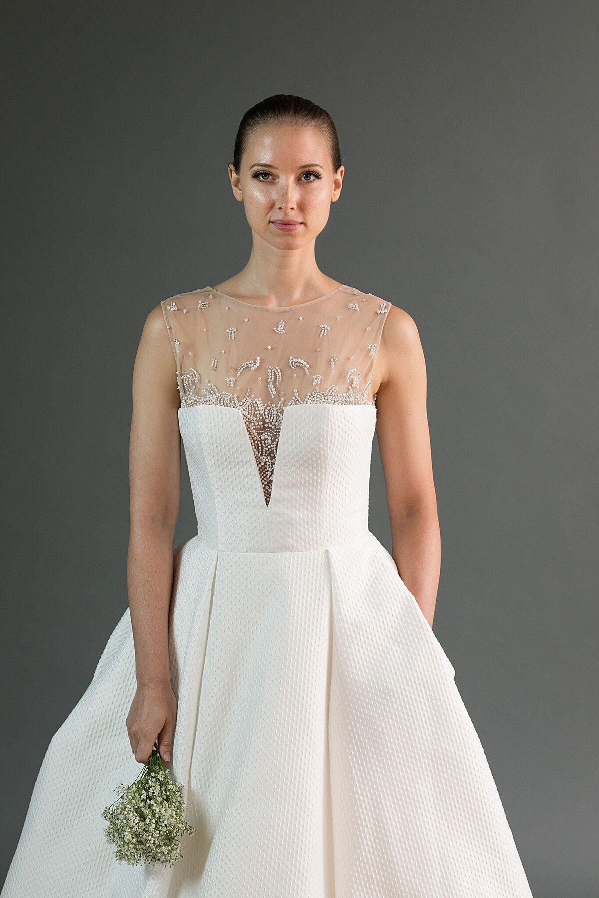 The notched V, low strapless bodice of the Kei wedding dress style sits on top of a hand-beaded illusion bodice.