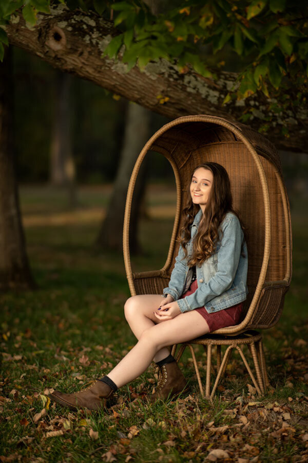girl outdoors in chair with fall leaves senior photos
