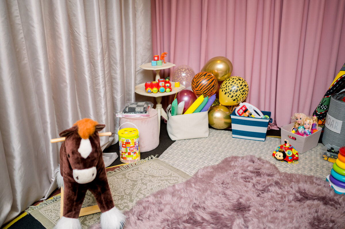Children's play area at a 50th wedding anniversary celebration, featuring blush satin draped walls, cozy area rugs, and a variety of toys for all ages. The thoughtfully designed space creates a welcoming and charming environment for young guests.