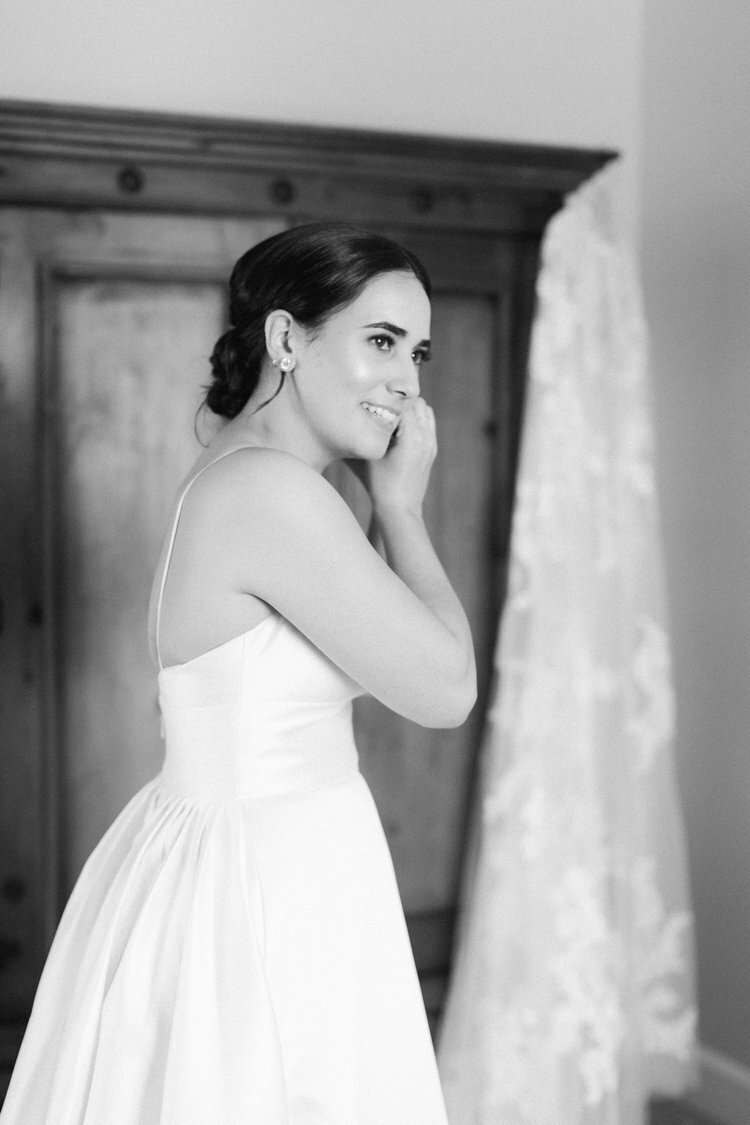 Black and white photo of bride putting her earrings in, wearing a strapless wedding dress