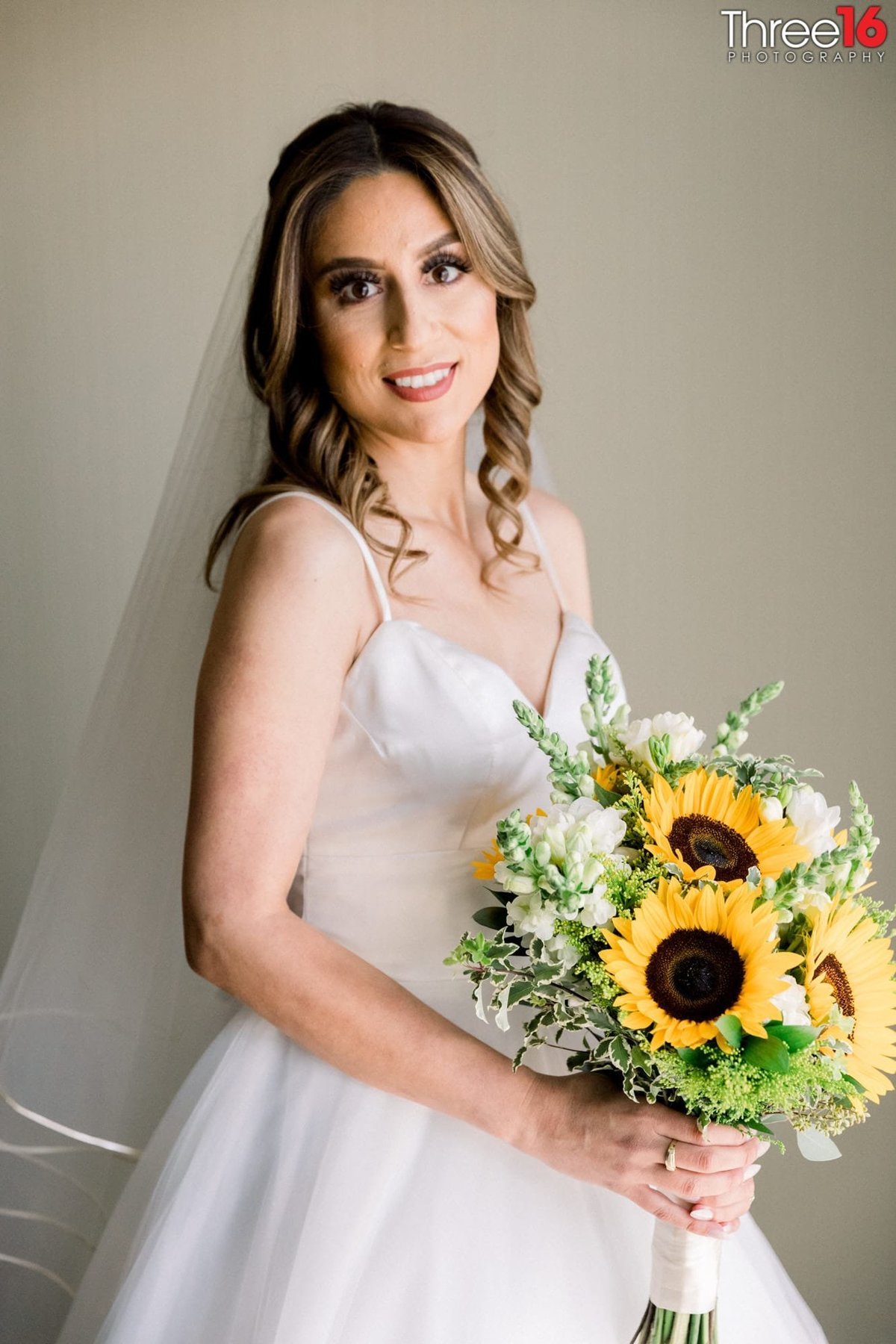 Bride poses before the ceremony holding her bouquet of flowers that includes sunflowers