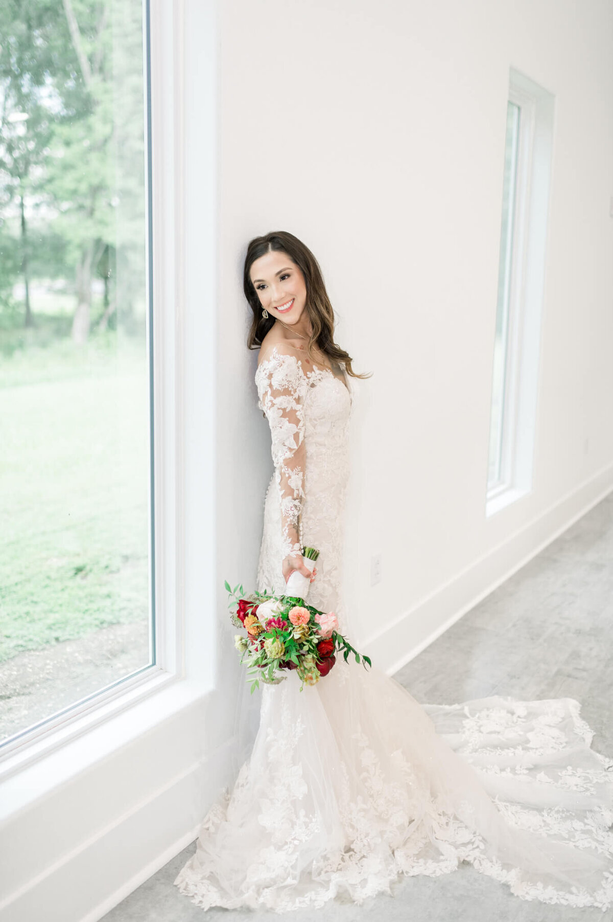 bride leans against the wall in fitted gown near window
