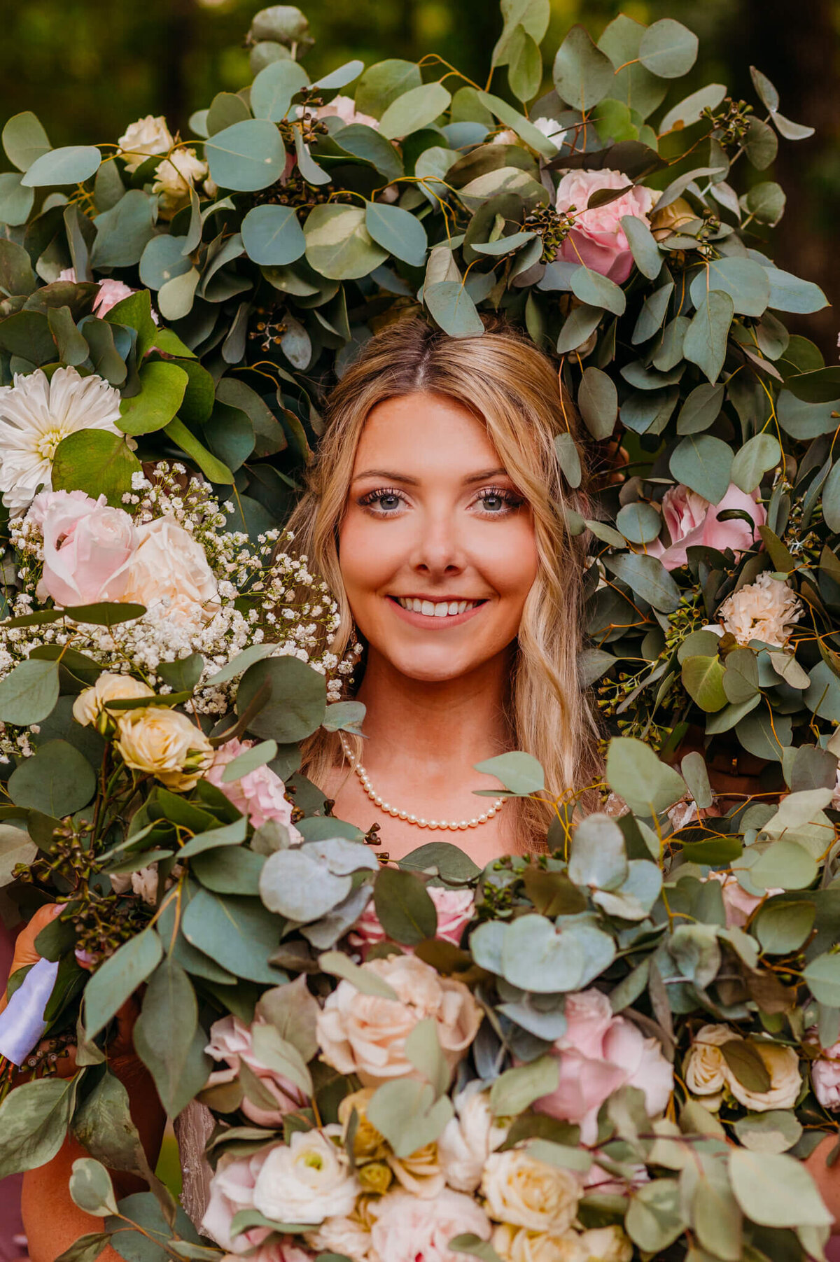 photo a bride wearing a Pearl necklace andsmiling while greenery and florals around her face