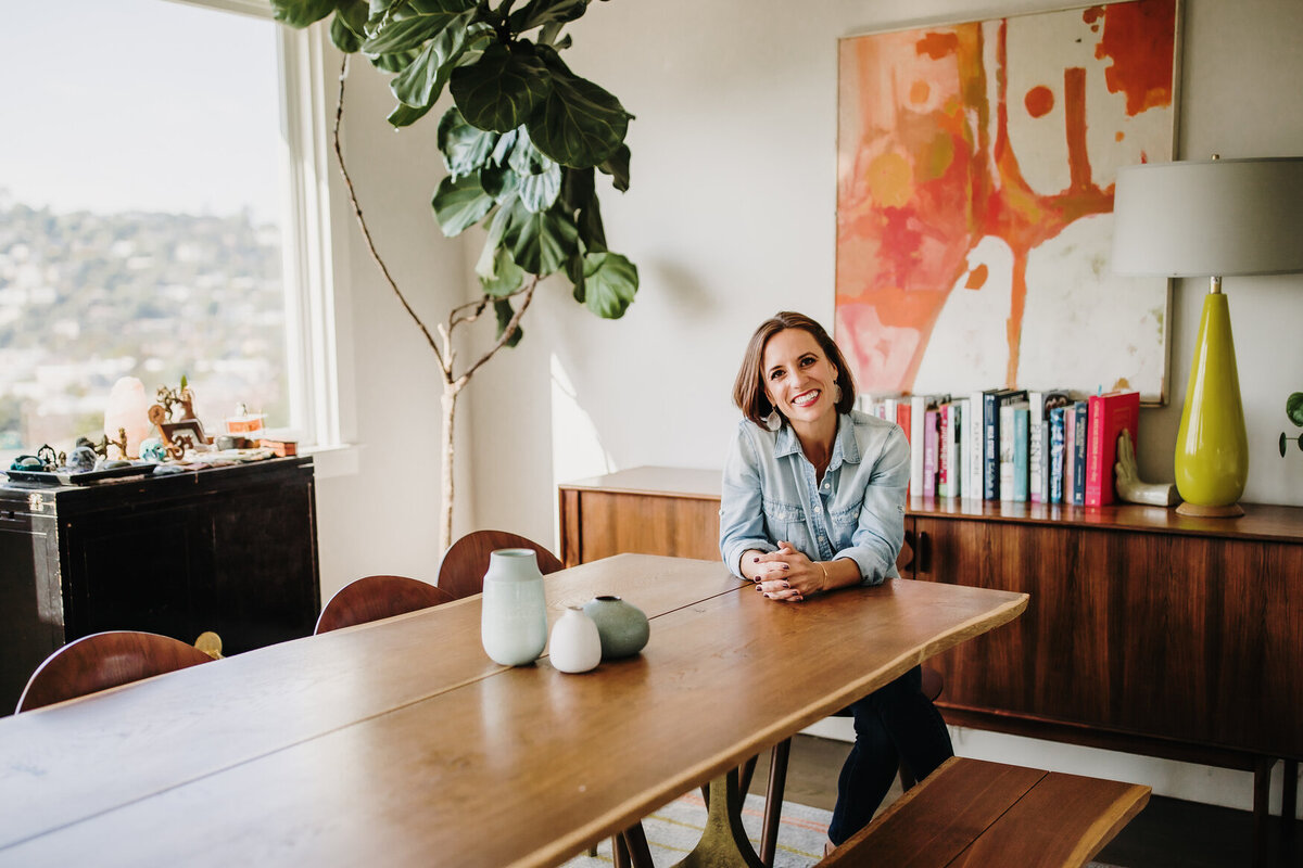 Bay Area lifestyle  headshot  of woman in her home at table with colorful art and books