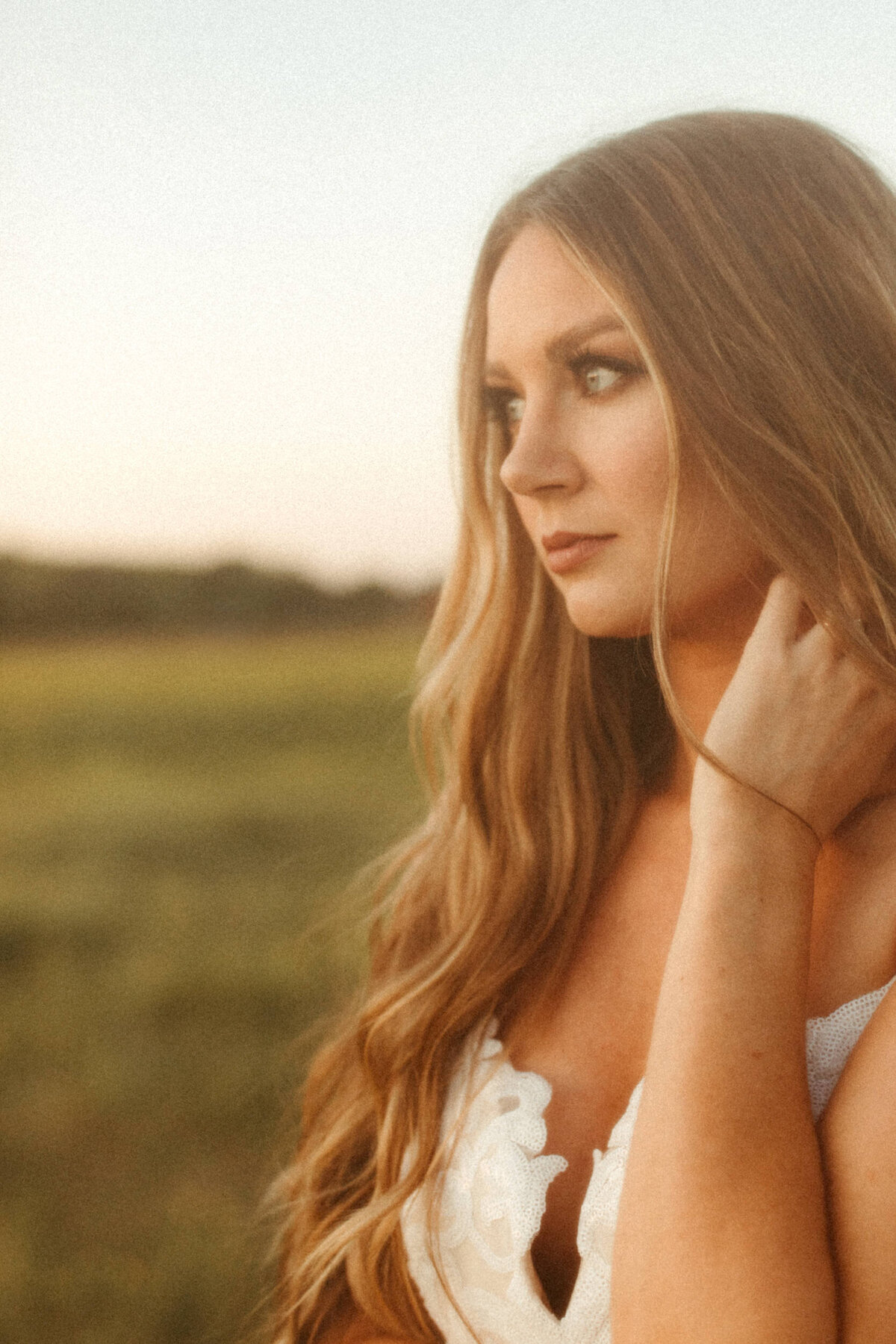 Film look of a boho bride looking off into the distance in a field at dusk