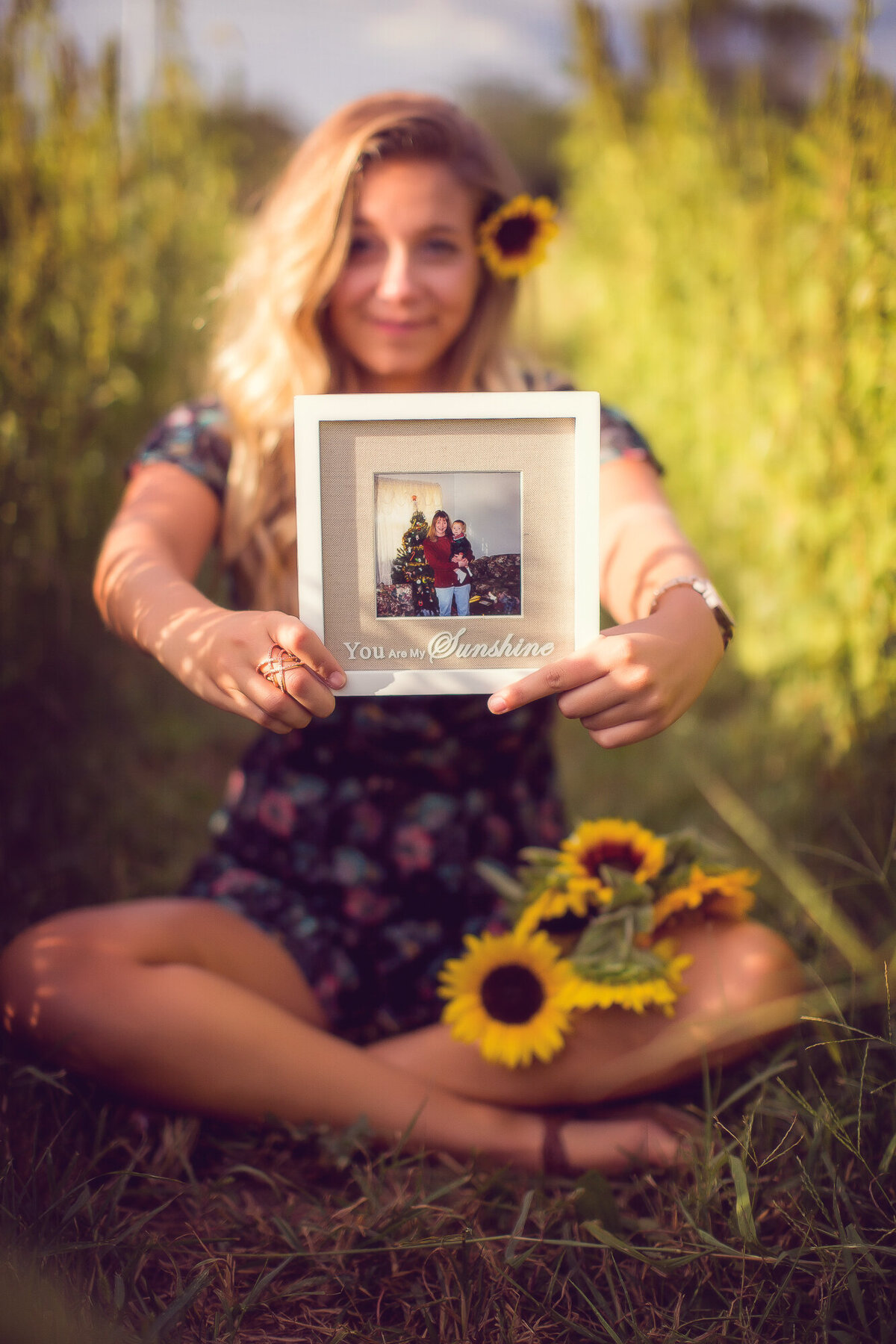 Girl in Sunflower field holding an image of her passed mom and herself