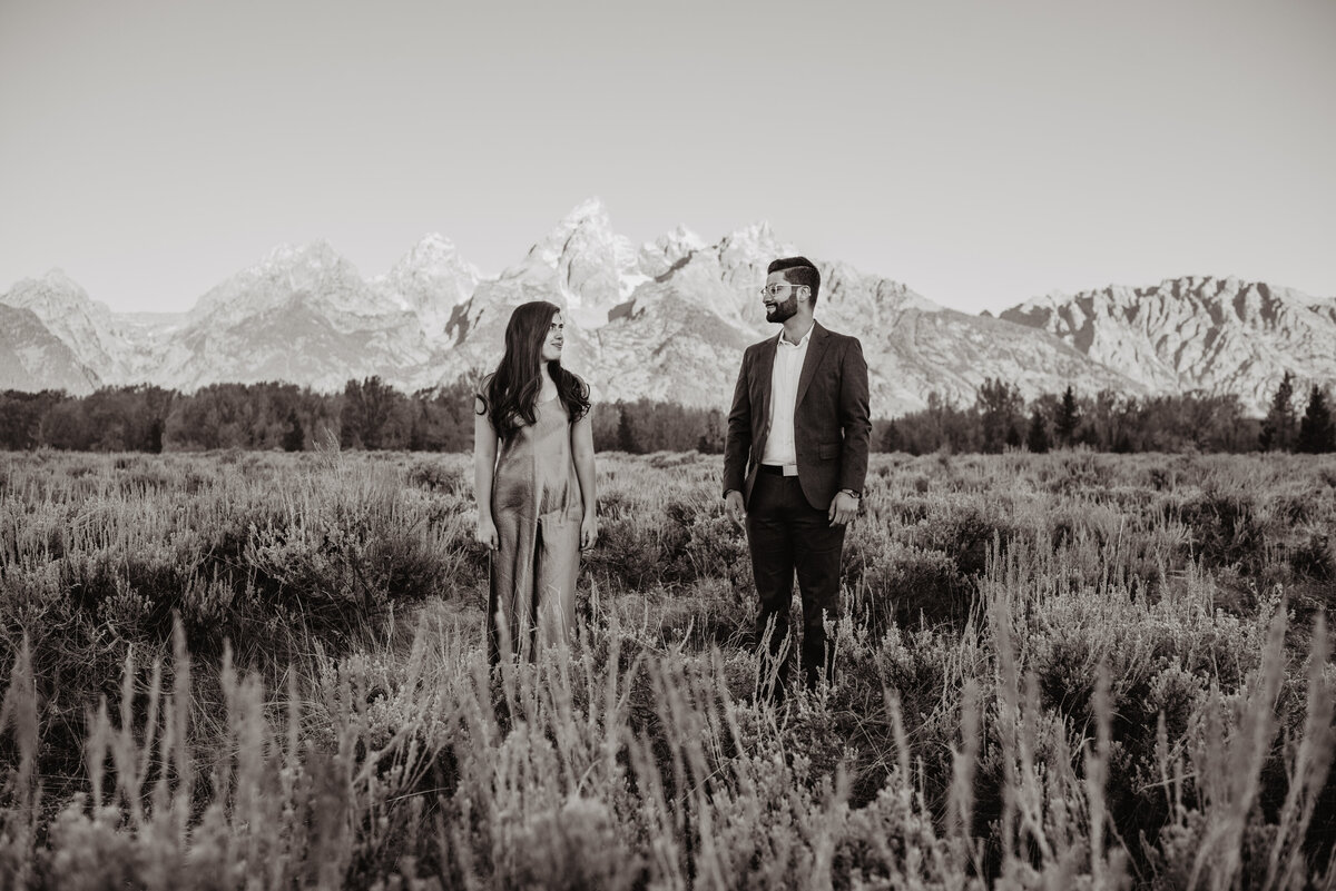 black and white photo of man and woman in Jackson Hole in a field looking at each other romantically captured by photographers in jackson hole