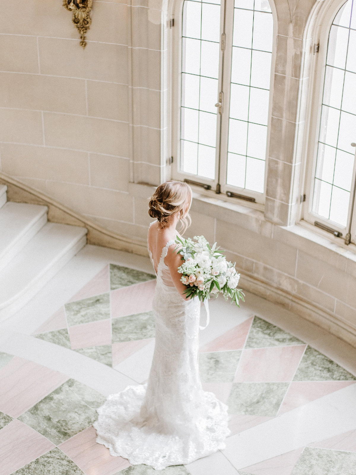 bride holding flowers facing a wall of windows
