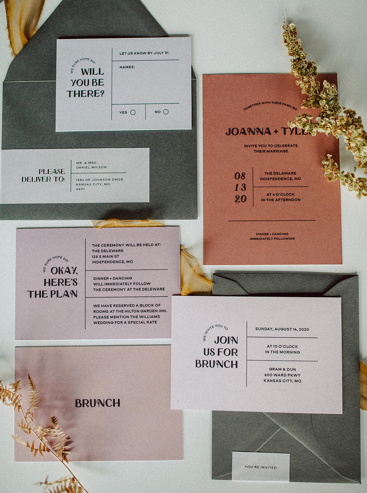 Various light gray, peach and mauve-colored wedding stationery with black font atop a white table with flower stems.