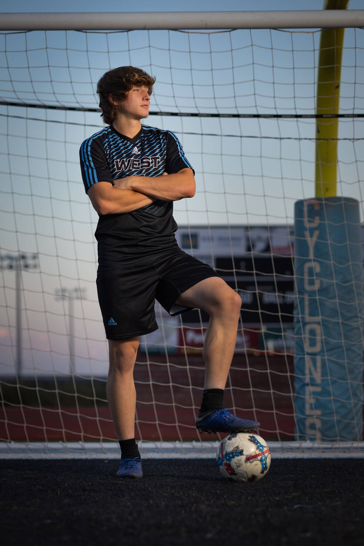high school senior boy wearing soccer uniform standing with soccer ball in a soccer net