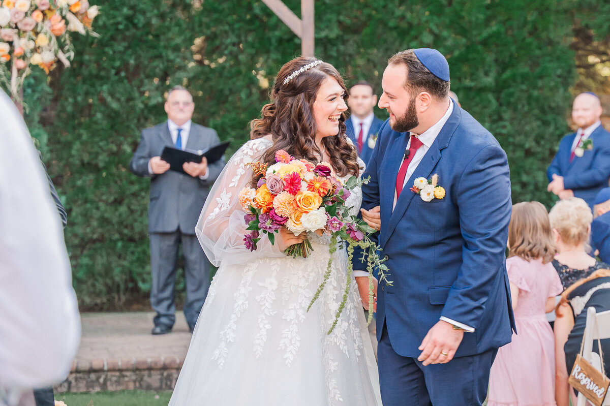 A bride and groom in a blue tux exiting their wedding ceremony while laughing under the fall leaves by Raleigh wedding photographer, JoLynn Photography