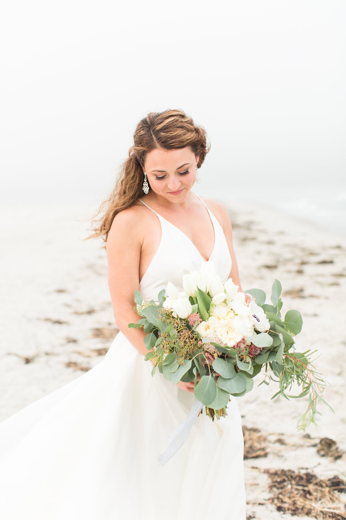 Bride looking at bouquet standing on coast of Maine