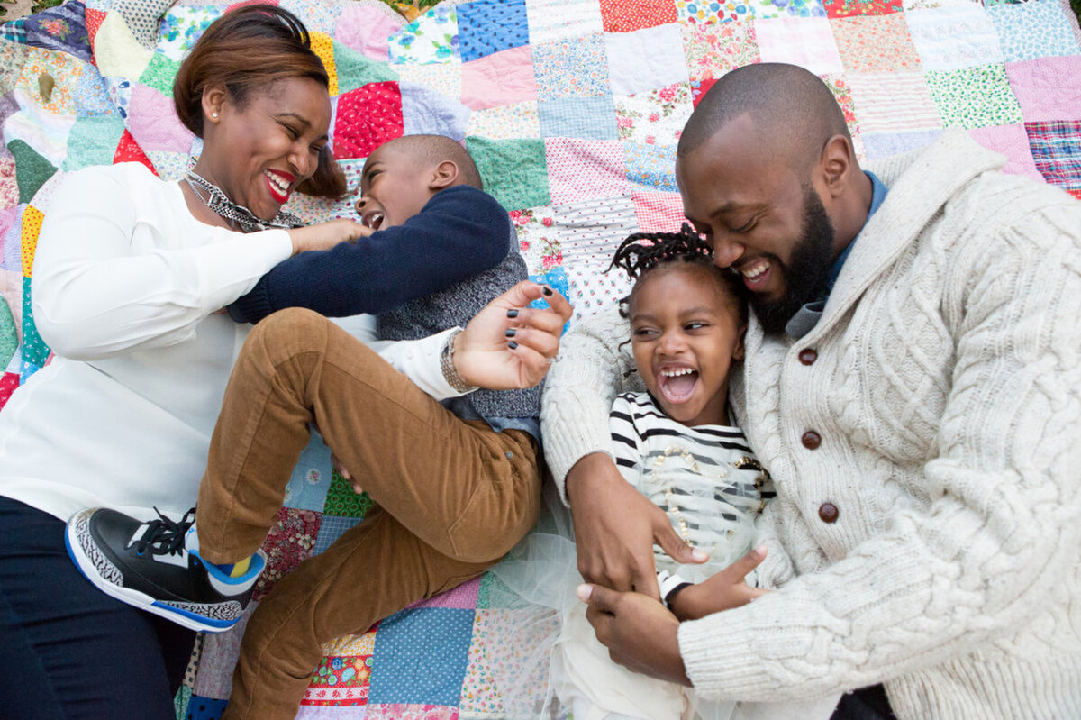 sleeping newborn baby boyA black family of four has a tickle fight on a patchwork quilt Brooklyn family photographer Milestone Images