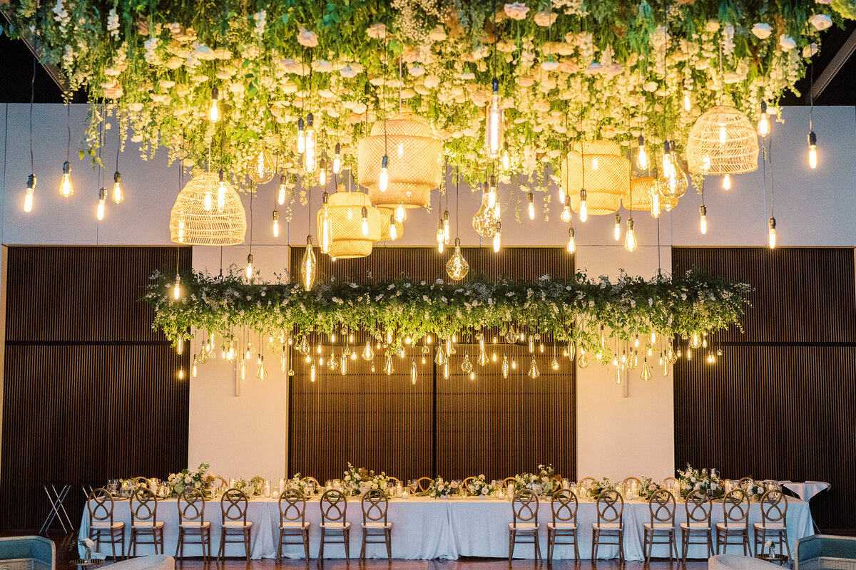 Large dance floor floral installation for classic summer wedding in downtown Nashville. Timeless floral design highlights this garden-inspired wedding reception. Hanging flowers and rattan chandeliers create lush floral dance floor moment. Classic white and green wedding with floral colors in cream, white, taupe, and champagne. Summer floral design full of roses, ranunculus, hydrangea, cosmos, and lisianthis. Design by Rosemary & Finch Floral Design.