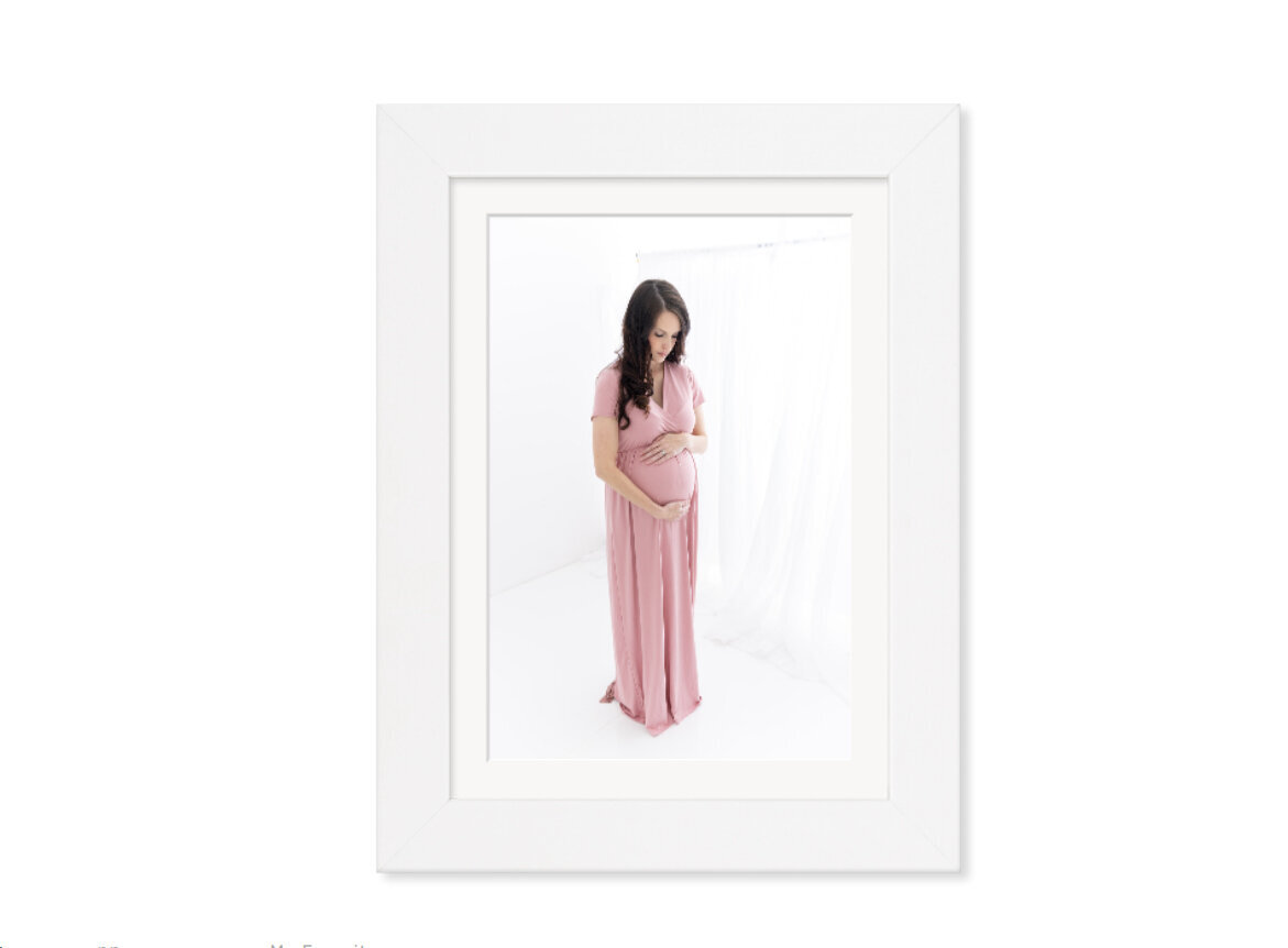 A framed fine art maternity photograph hangs on a wall
