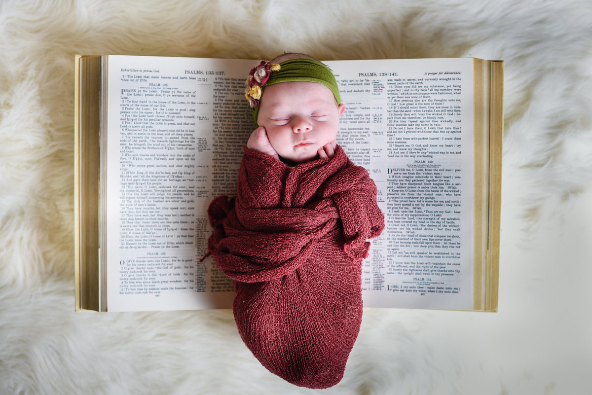 Beautiful Mississippi Newborn Photography: newborn baby girl wrapped in burgundy with floral headband laying on family Bible