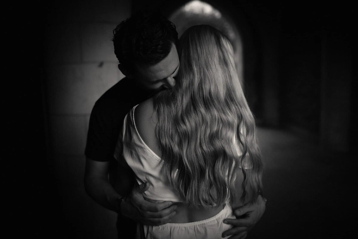 A couple in a dimly lit tunnel, sharing a hug, with the woman's long hair cascading down as they stand close together.